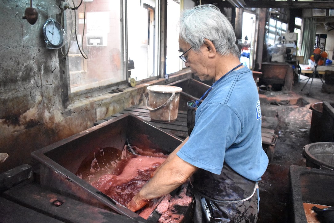 Hand-dyeing silk threads in sharinbai liquid  during the traditional dyeing process in Amami Oshima