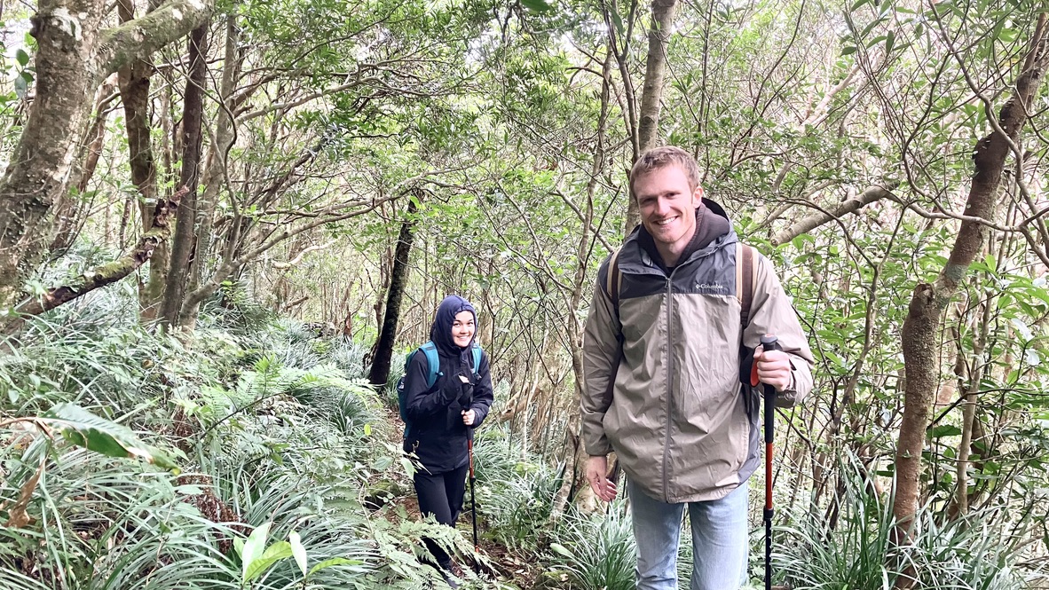 Two hikers walking through a narrow mountain trail in the Amami forest