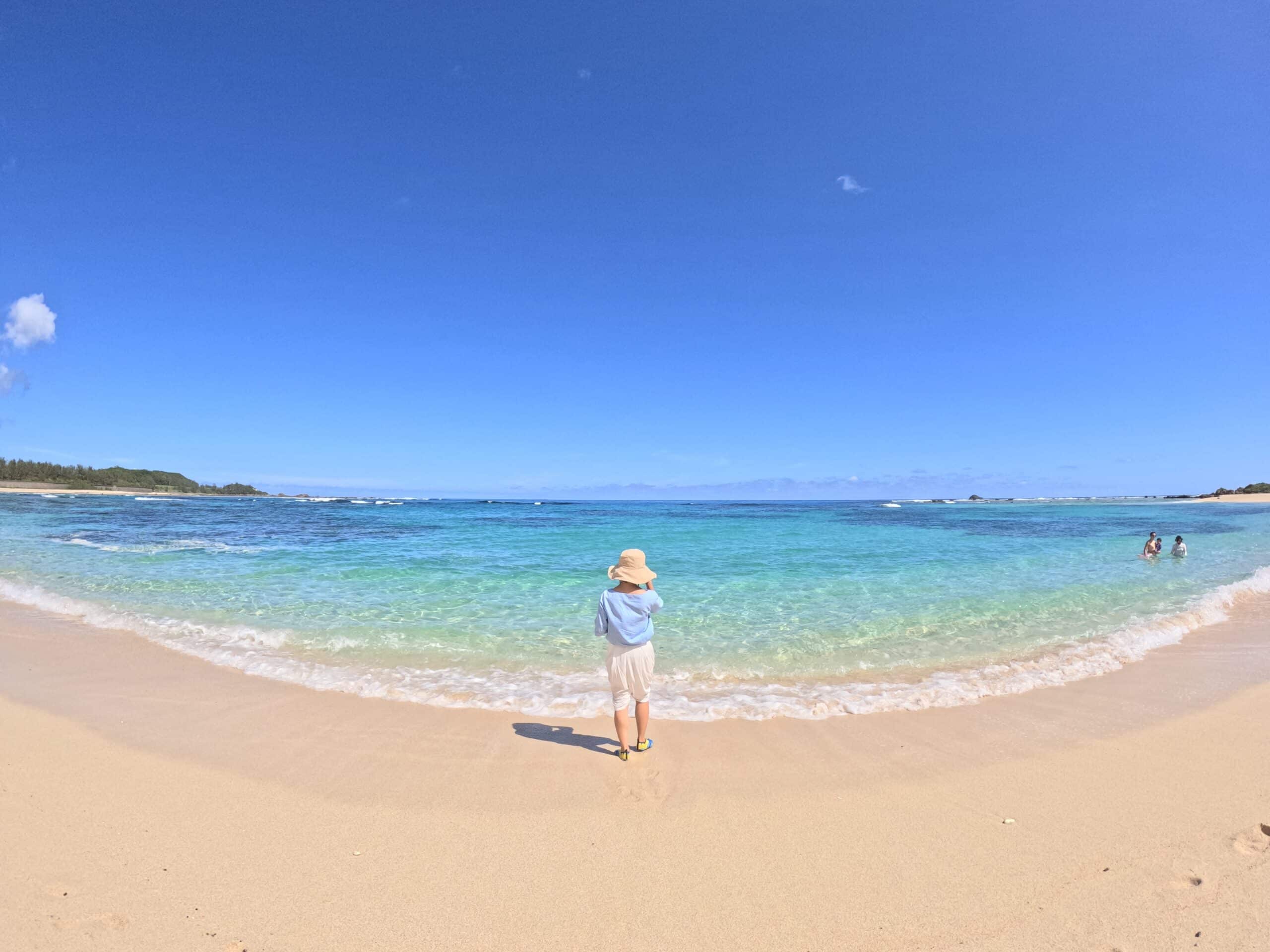 A young girl stands on the shore looking at the clear blue sea on a sunny day in Tomori beach, Amami Island.