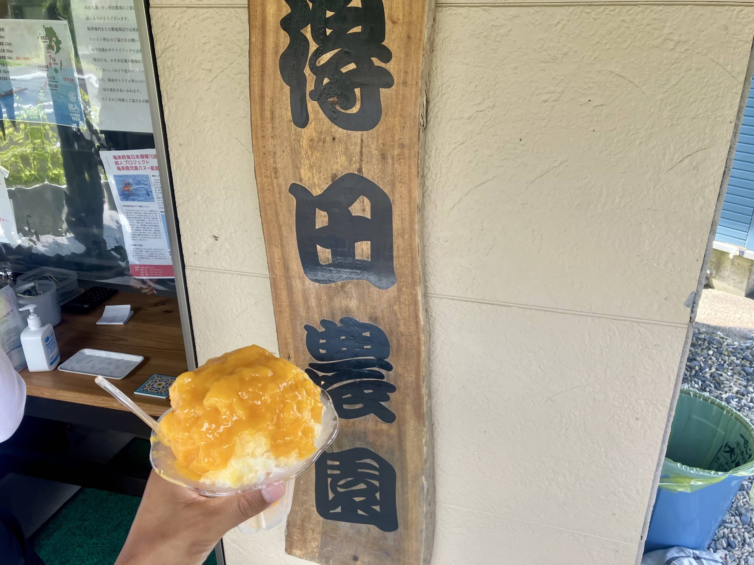 Fresh mango shaved ice in front of a local fruit cafe sign in Amami Oshima