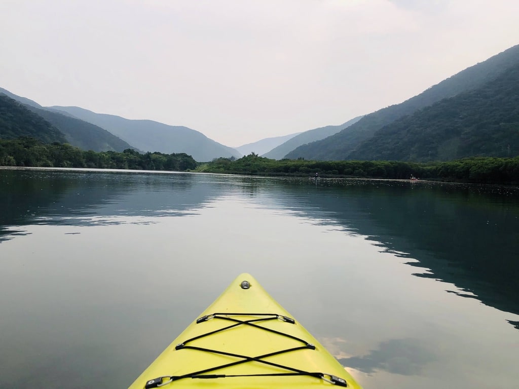View from a kayak gliding across the river in Amami Oshima, with mangrove forest and misty mountains in the distance.